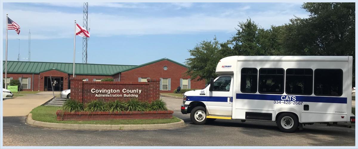exterior photo in front of the Covington County Administration building, a sunny day, with the brick sign and a small CATS bus next to it. 